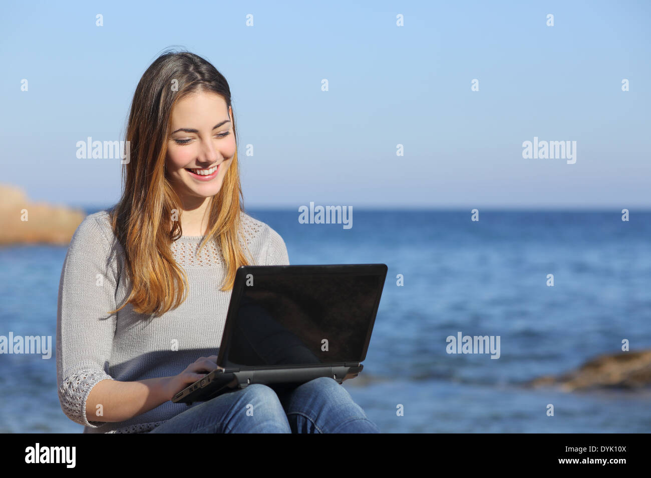 Glücklich Teenager Mädchen Surfen social Media auf den Strand mit dem Meer im Hintergrund Stockfoto