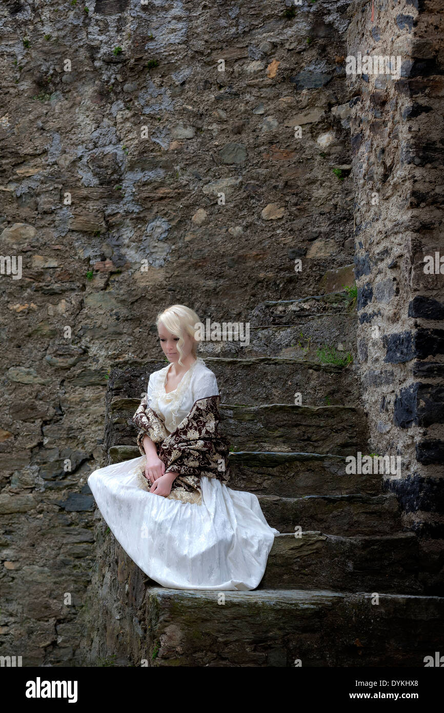 eine Frau in einem weißen Periode Kleid sitzt auf alten Steintreppen Stockfoto