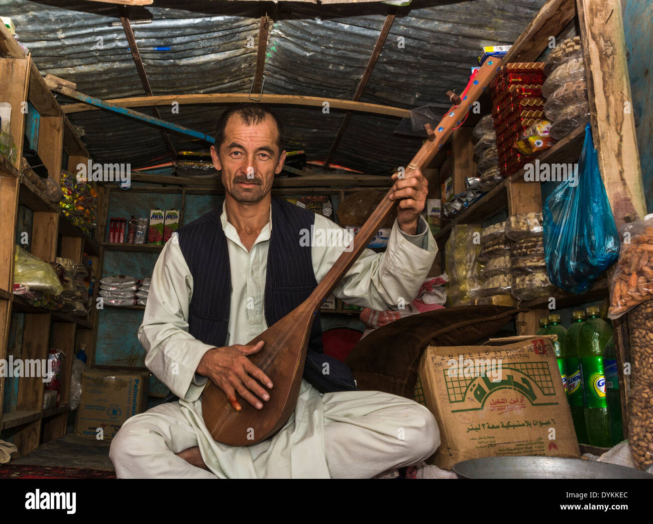 Ladenbesitzer und Musiker in Samangan (Afghanistan), sitzt in seinem kleinen Laden üben sein traditionelles Saiteninstrument Stockfoto