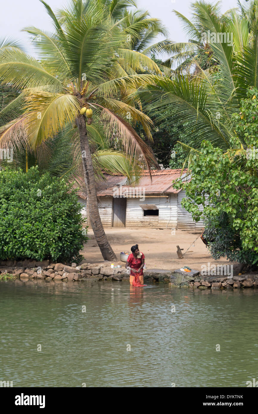 Eine junge Frau, die Wäsche in einer Wasserstraße vor ihrem Haus in den Backwaters in Kerala, Indien Stockfoto