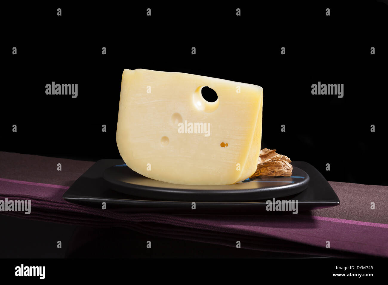 Kulinarischen luxuriösen Käse Stillleben. Emmentaler Käse Stück auf schwarze Platte auf schwarzem Hintergrund isoliert. Kulinarischen Käse Essen Stockfoto