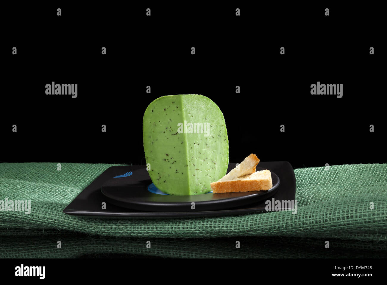 Grüne Gouda-Käse auf grüne Tischdecke auf schwarzem Hintergrund. Kulinarischen luxuriösen Käse essen. Stockfoto