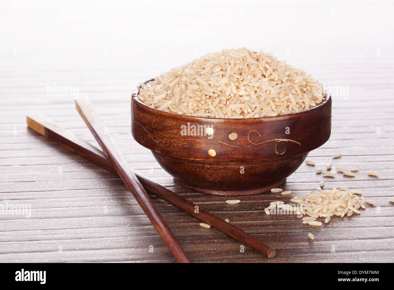 Luxuriöse Reis Hintergrund. Rohe braune Reis ungeschält in asiatischen Runde Holzschale auf braunem Hintergrund. Kulinarischen asiatisch Essen. Stockfoto