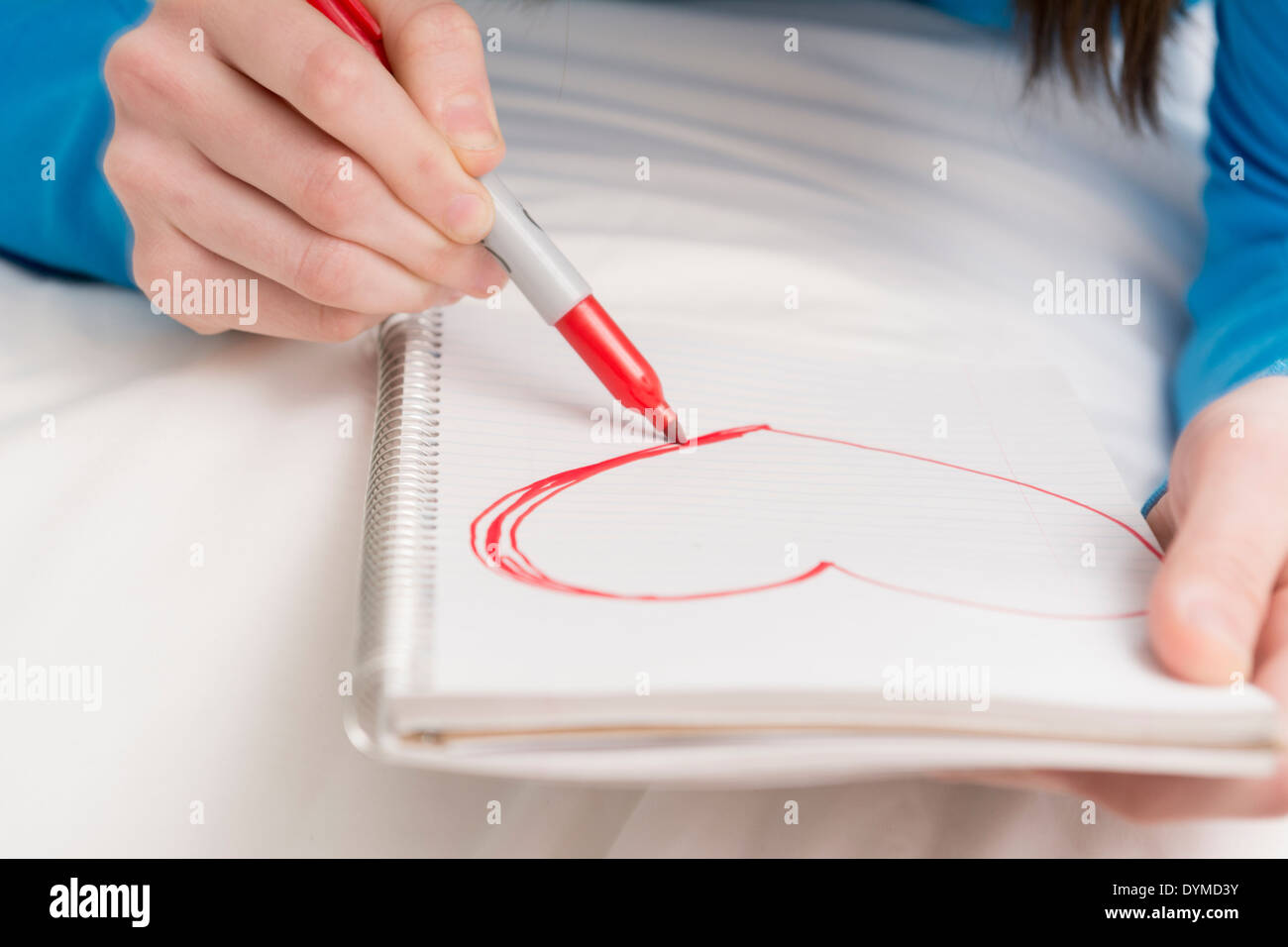 Teenager-Mädchen zeichnen rotes Herzform im Notizbuch oder Journal in Nahaufnahme Stockfoto