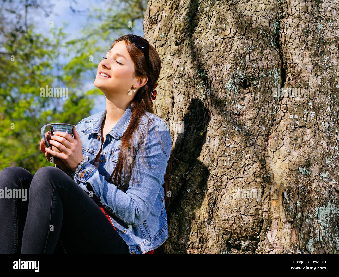 Foto von einer schönen jungen Frau, die die Wärme der Sonne im Vorfrühling genießen, während sie ihren Kaffee trinkt. Stockfoto