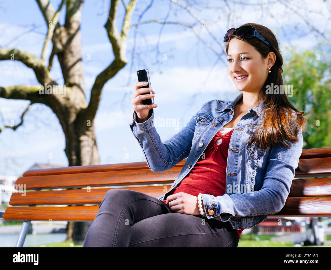 Foto von einer schönen jungen Frau, die mit einem Smartphone beim Sitzen auf einer Parkbank. Stockfoto
