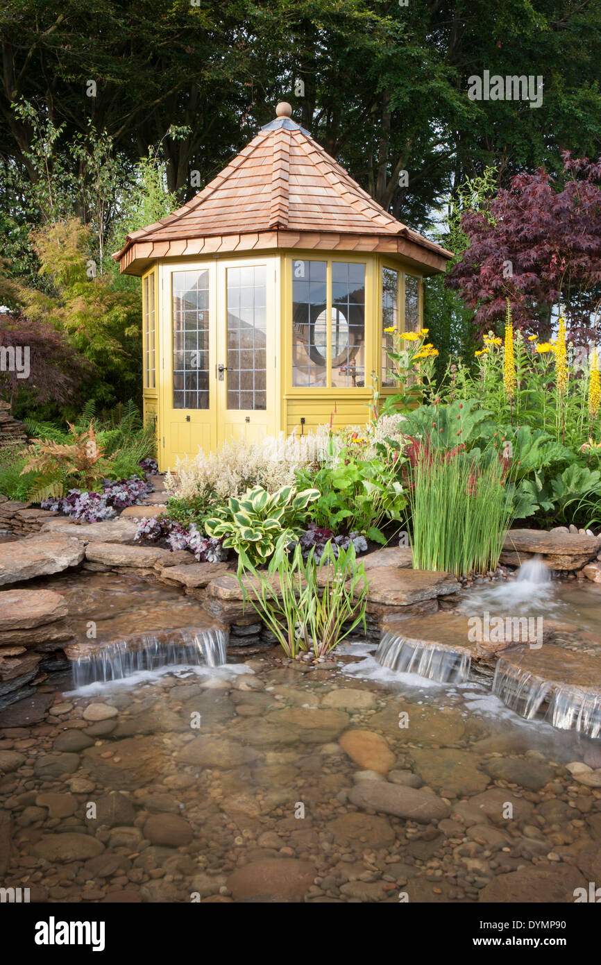 Ein Land Vorstadtgarten im Sommer mit einem Sommerhaus Sommerhaus Hütte kleinen Teich Wasserspiel mit Wasserfall und bunte Blumen gemischt Grenze Großbritannien Stockfoto