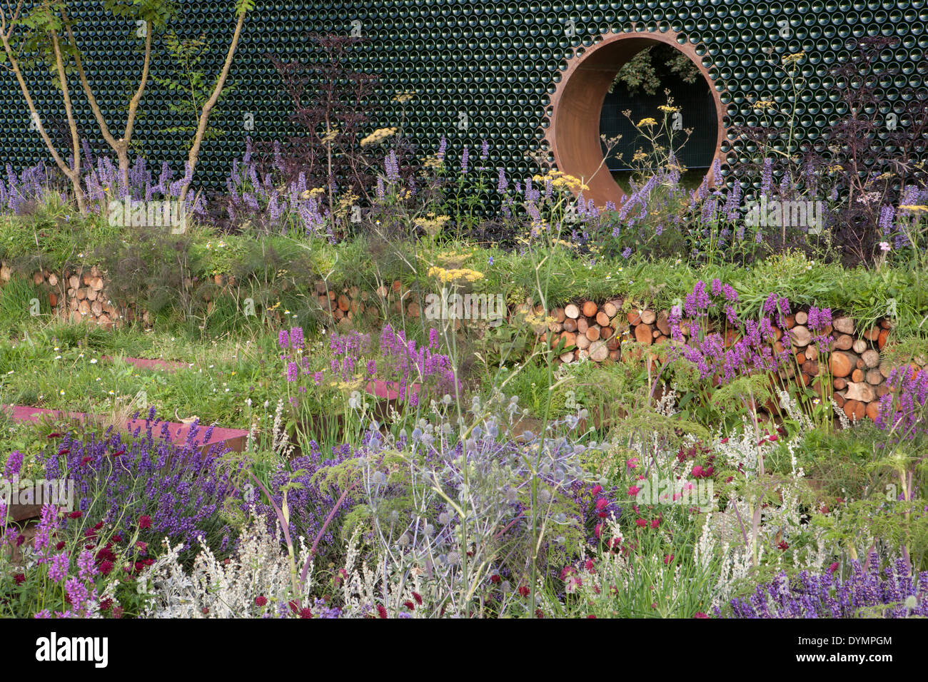 Ein kleiner, umweltfreundlicher Gartenzaun mit alten, wiederverwendeten Flaschen, insektenfreundlichen Stämmen, Pflanzen von Kräutern und Wildblumen UK Stockfoto