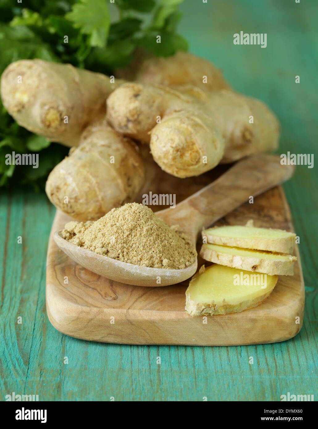 gemahlener Ingwer in einem hölzernen Löffel, frische Wurzel im Hintergrund Stockfoto