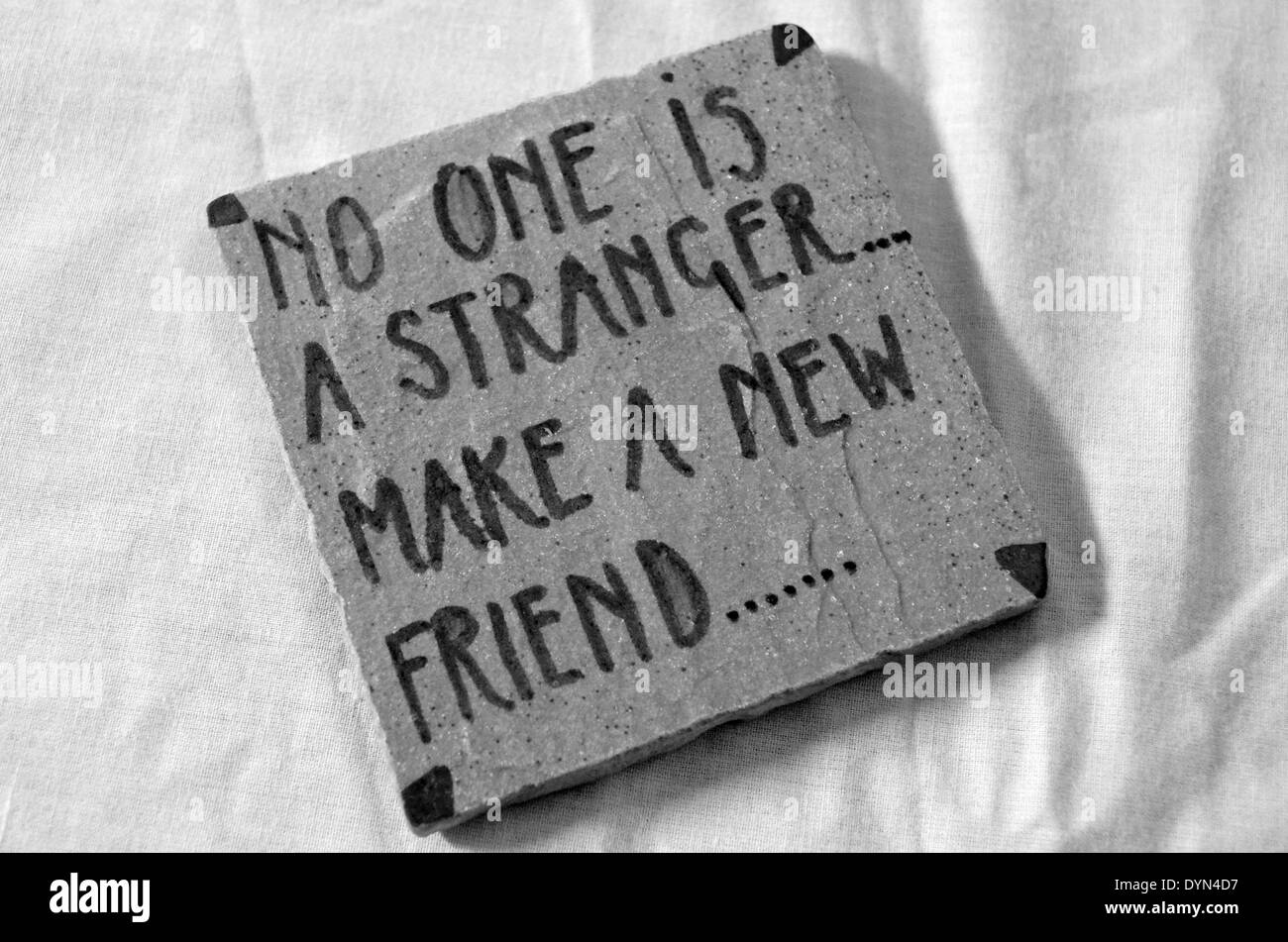 Eine Kachel mit einer Beschriftung "Niemand ist ein Fremder... machen Sie einen neuen Freund...". Schwarz & weiß, auf einem Tisch decken Stockfoto