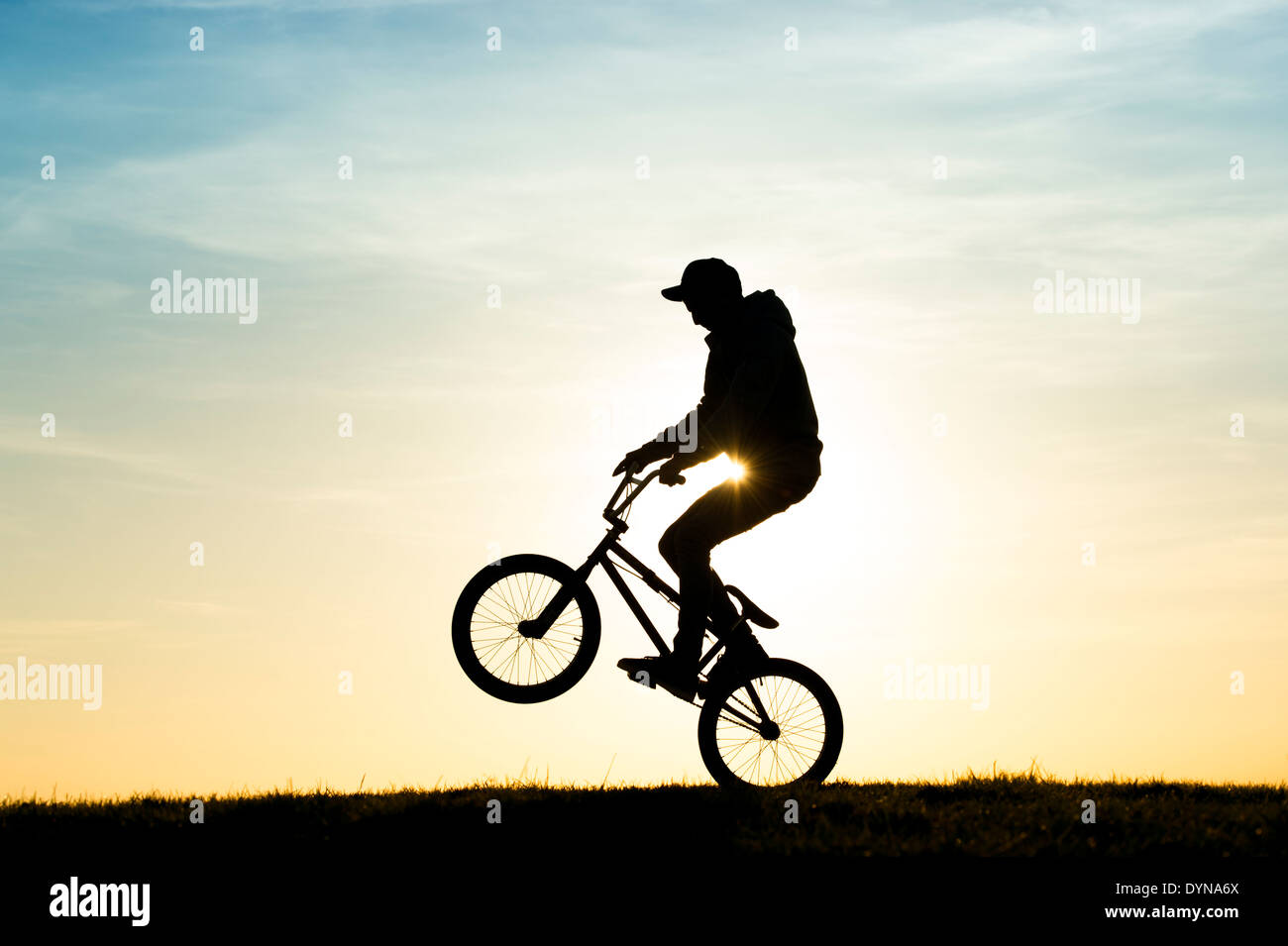 Junger Mann einen Wheelie auf seinem BMX-Fahrrad zu tun. Silhouette Stockfoto