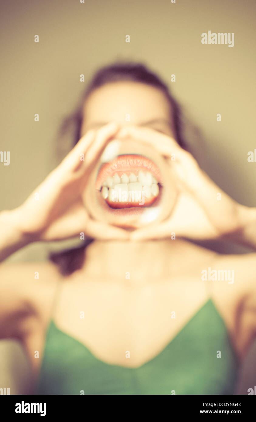 Junge Frau mit Lupe vor Mund, zeigt ihre Zähne. Stockfoto