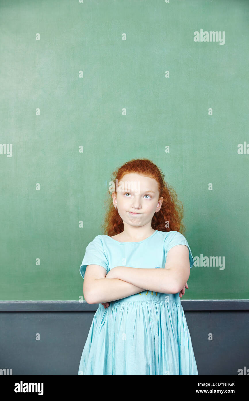 Nachdenkliche Mädchen vor einer Tafel in der Grundschule Stockfoto