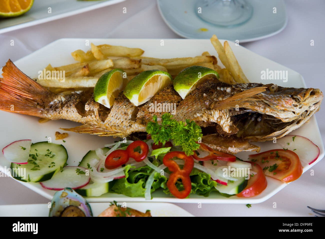 Ein gebratener ganzer Fisch in einen Teller mit frischem Gemüse serviert. Stockfoto