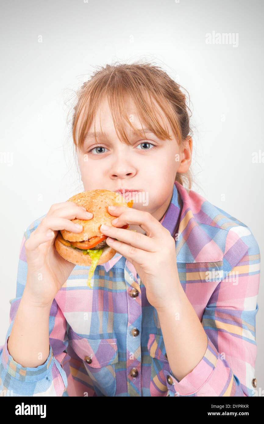 Kleines blondes Mädchen isst Burger über weiße Wand Stockfoto