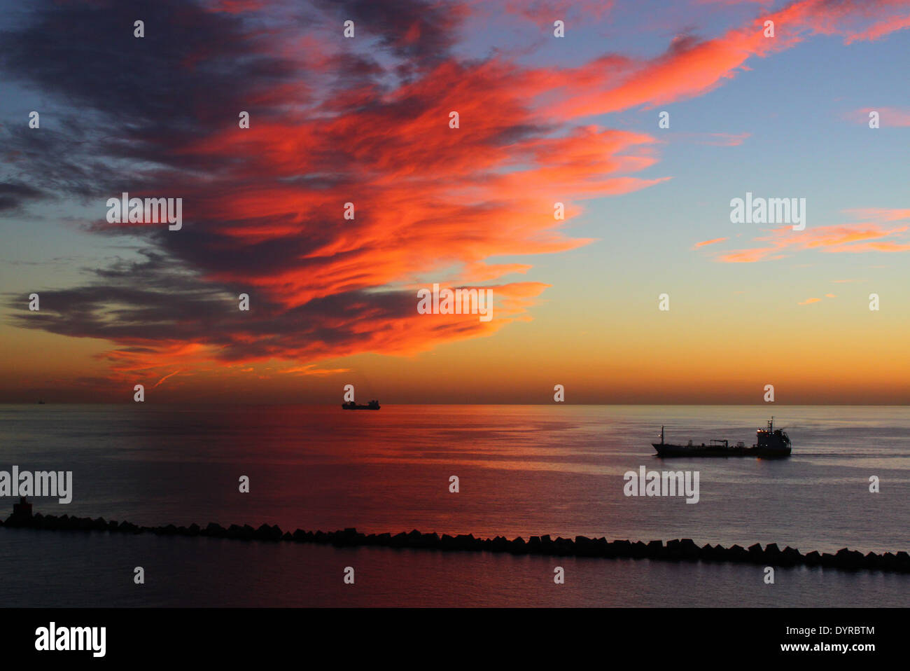 Sonnenaufgang im Hafen von Las Palmas de Gran Canaria, Spanien, mit dramatischer Himmel, rote Wolken und drei Schiffe in Sicht Stockfoto