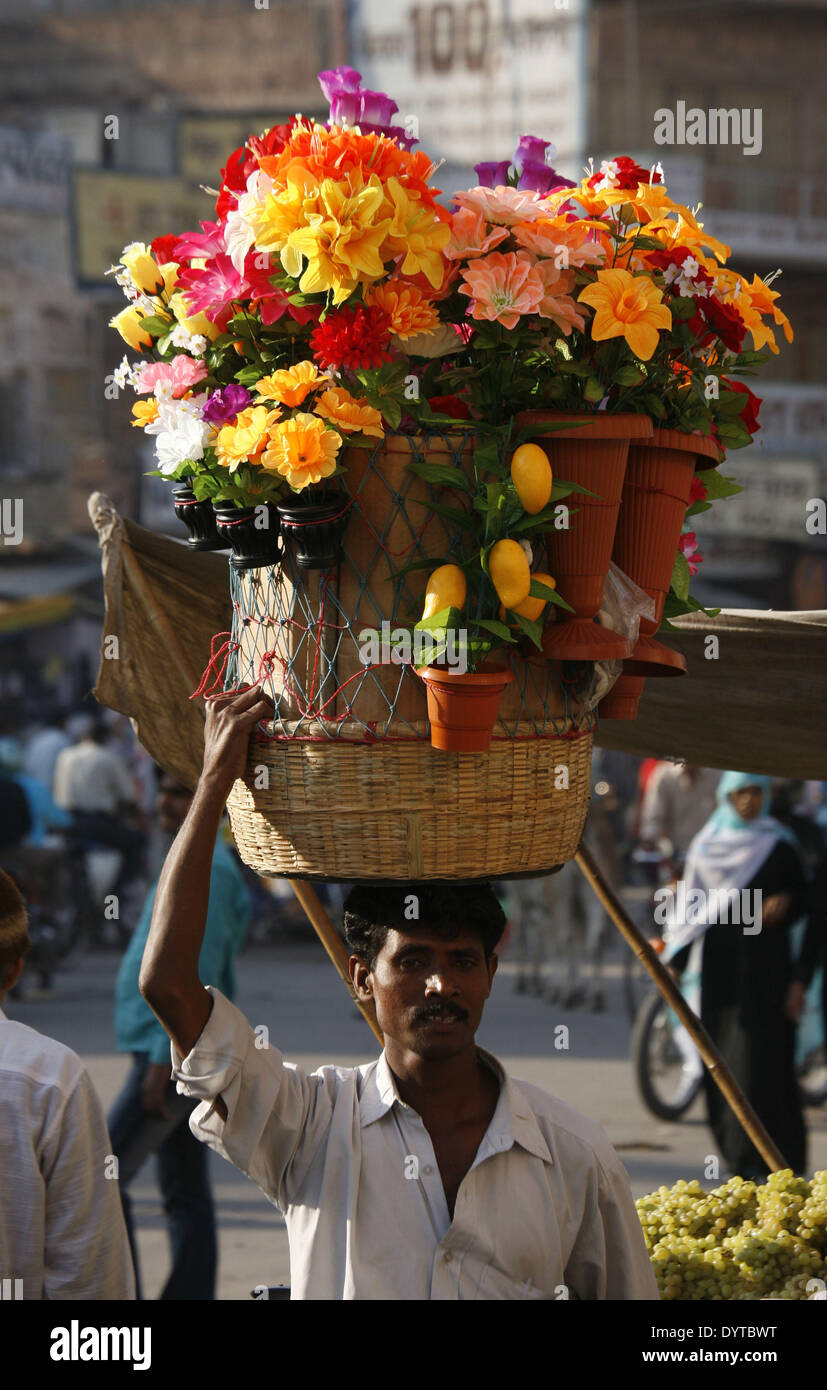 Eine Straße Verkäufer trägt Plastikblumen auf dem Kopf auf einem Markt von Jodhpur Stockfoto