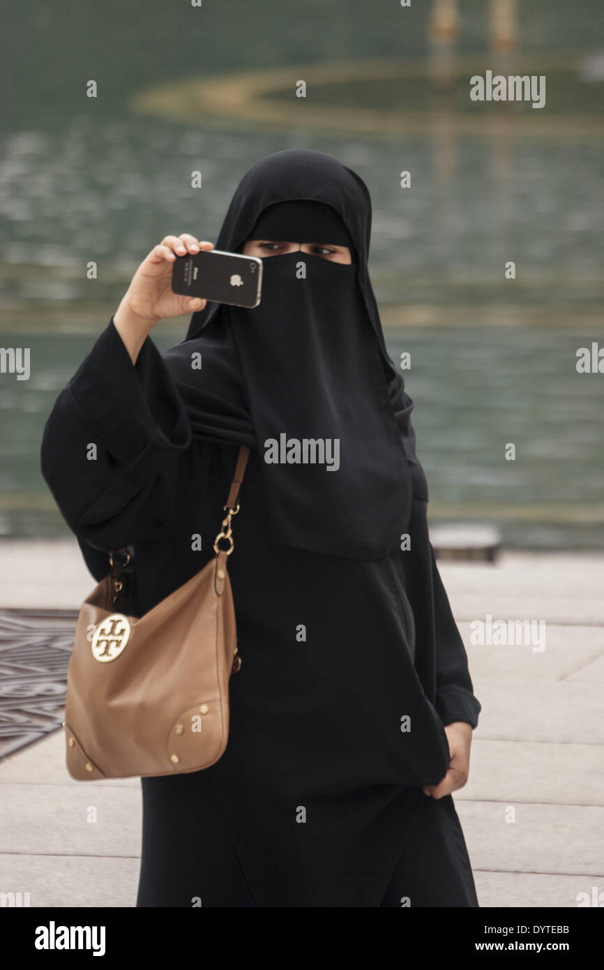 Eine muslimische Frau nutzt ihr Apple Iphone, ein Bild auf einer Straße Stockfoto