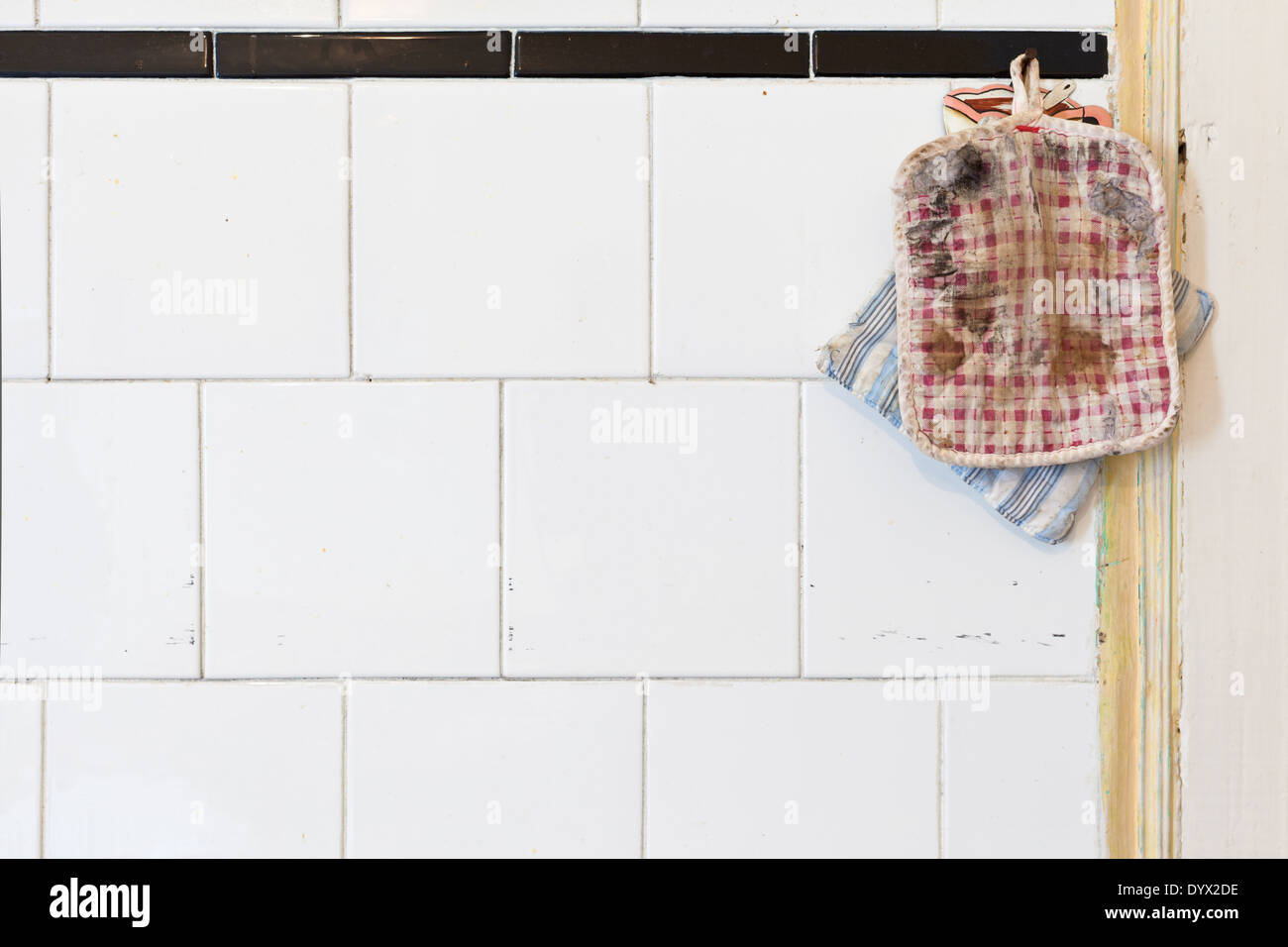 Zwei alte Topflappen auf einem schmutzigen weißer geflieste Küchenwand. Viele Textfreiraum Stockfoto