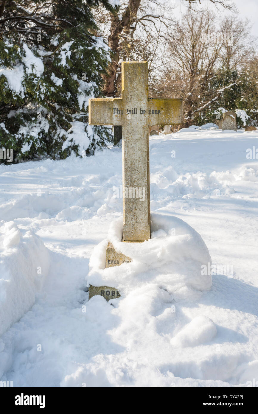 Grabstein in Form eines Kreuz eingeschrieben "Dein Wille geschehe" an der Kirche des Heiligen Nikolaus, Pyrford, Surrey, UK im Schnee im Winter Stockfoto