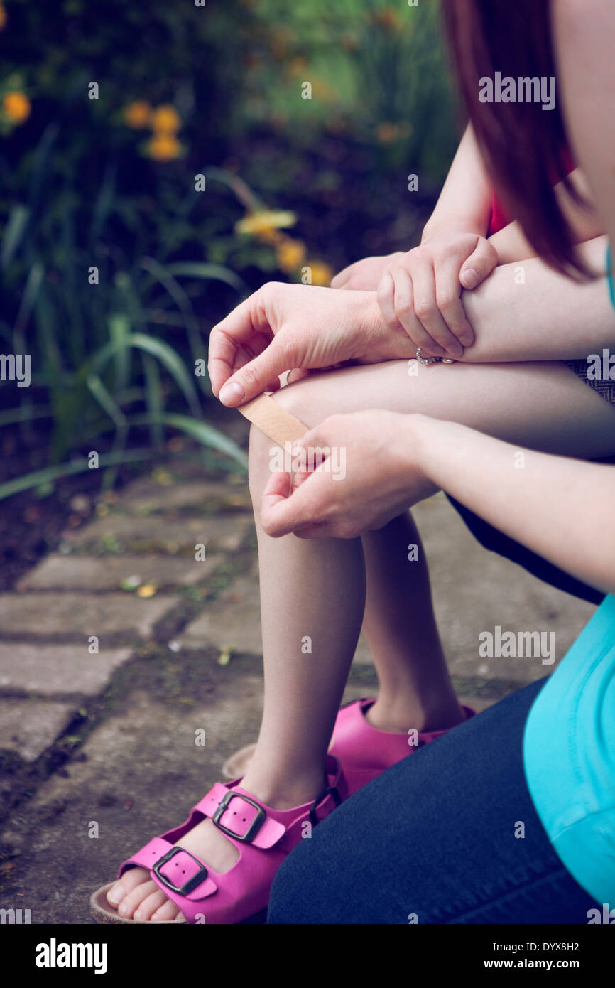 Nahaufnahme eines Erwachsenen, ein Pflaster auf ein Kind Knie. Stockfoto