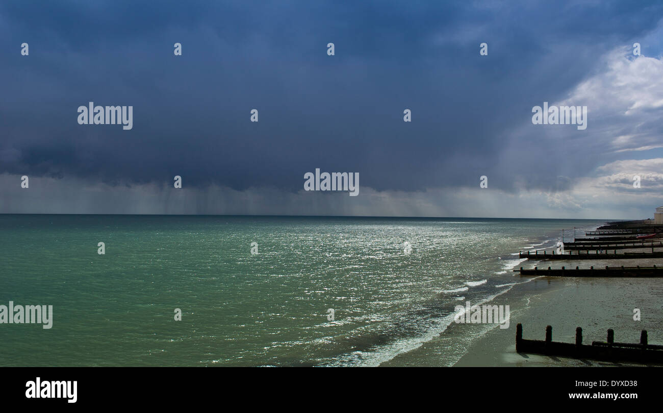 hohen weiten Blick auf der Suche nach einem leeren Strand bei Ebbe mit verwitterten hölzernen Ozean Barrieren, dramatischer Himmel & Regen am Horizont Stockfoto