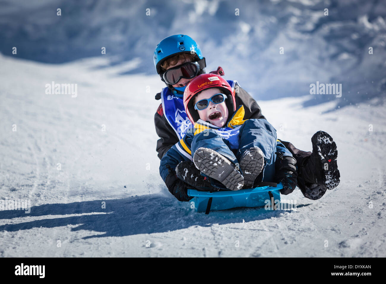 Zwei kleine Kinder lachen und schreien, als sie einen verschneiten Hang hinunter rodeln. Stockfoto