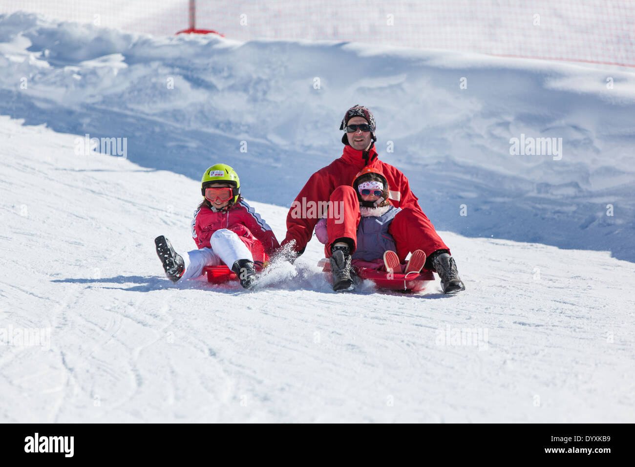 Kinder lachen, als sie mit einem Erwachsenen einen verschneiten Hang hinunter rodeln. Stockfoto