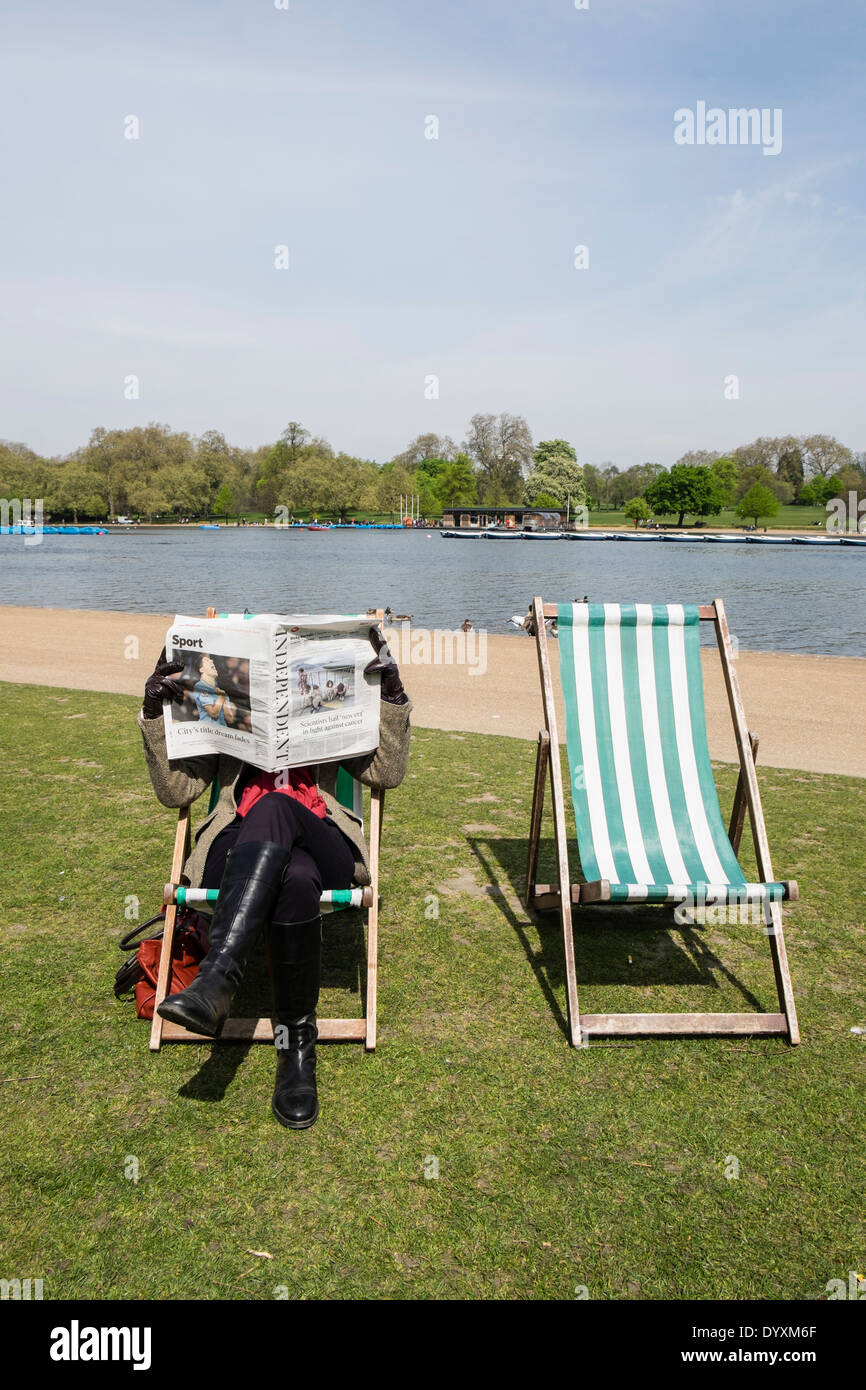 Frau liest eine Zeitung sitzt auf einem Liegestuhl im Hyde Park in London Vereinigtes Königreich Stockfoto