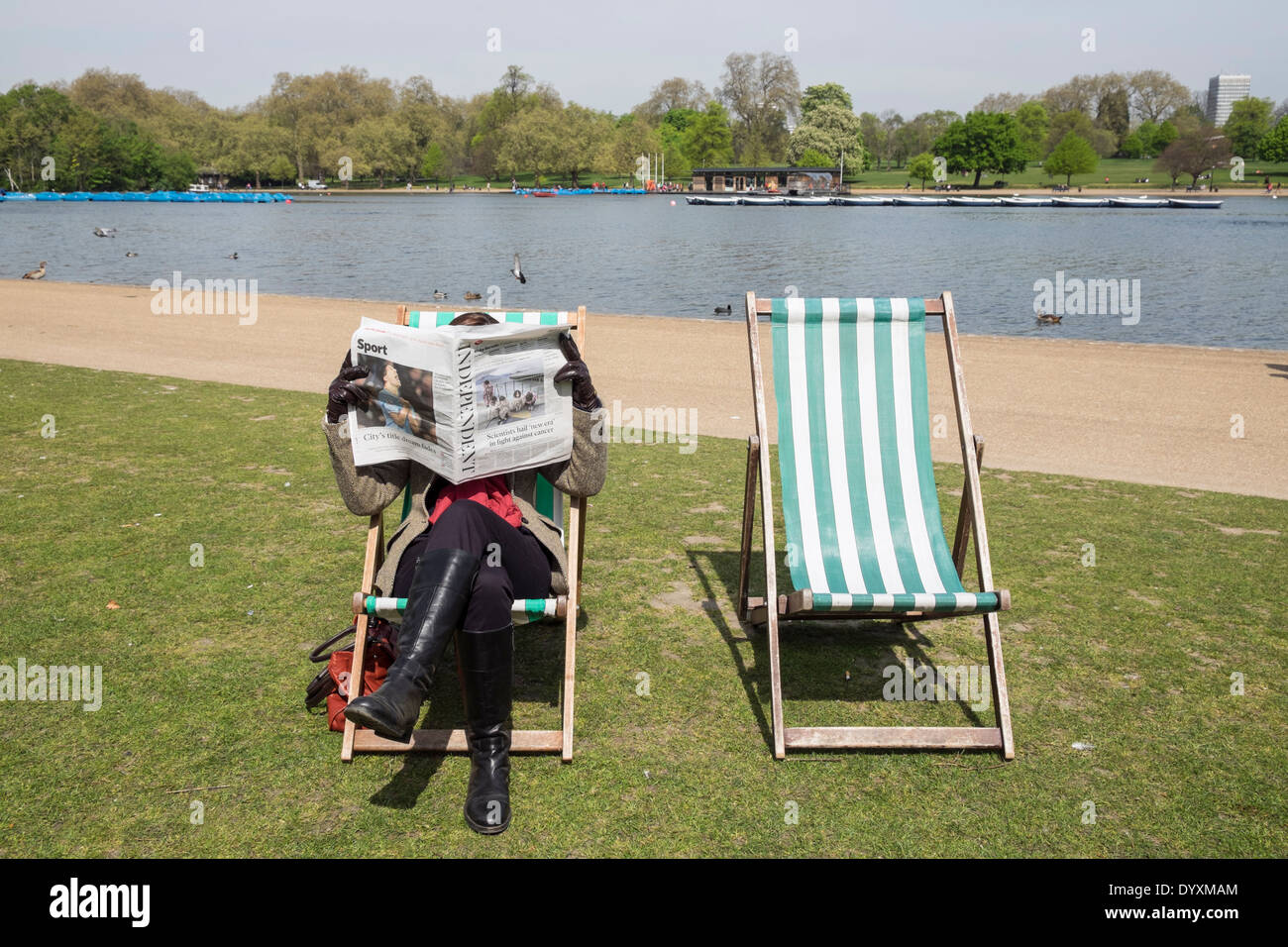 Frau liest eine Zeitung sitzt auf einem Liegestuhl im Hyde Park in London Vereinigtes Königreich Stockfoto