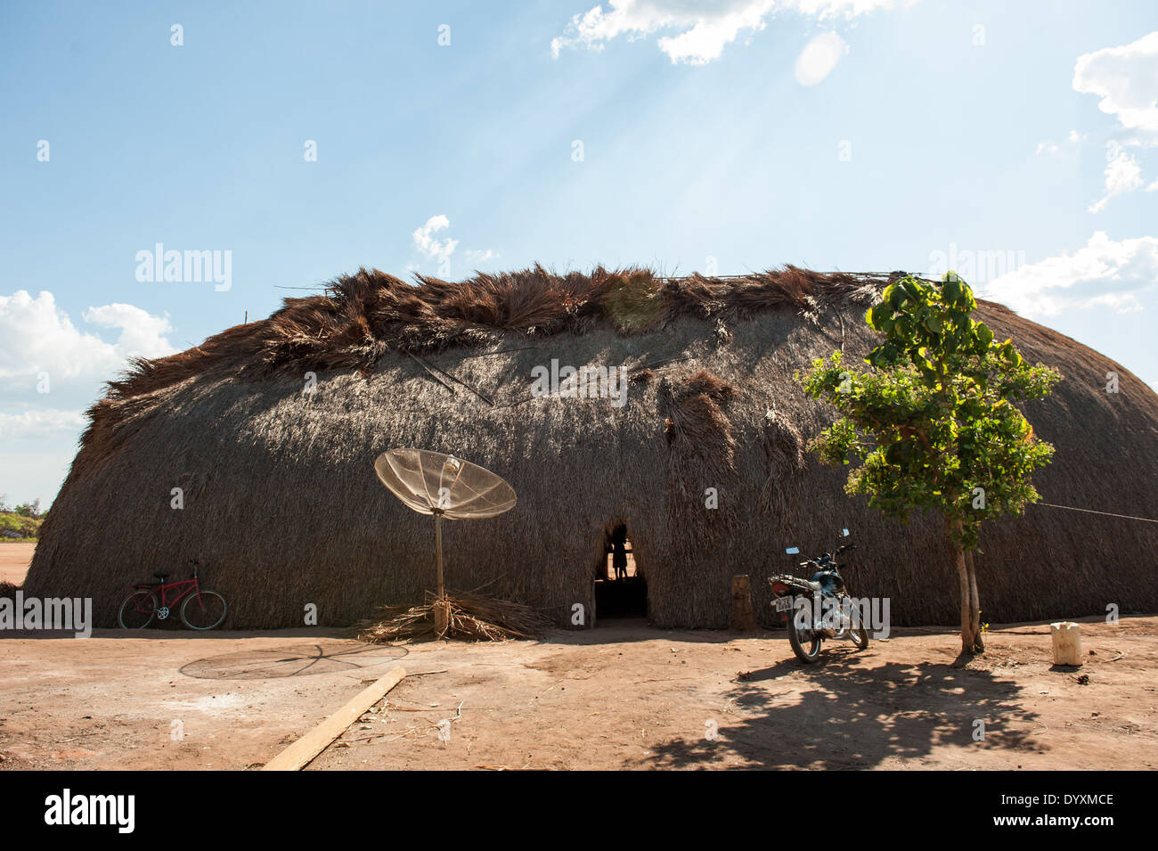 Xingu indigenen Park, Mato Grosso, Brasilien. Aldeia Matipu. Traditionelle Oca Einfamilienhaus, Fahrrad, Satelliten-Schüssel, Motorrad und Baum. Kombination von traditioneller Kultur und neuen Technologien. Stockfoto
