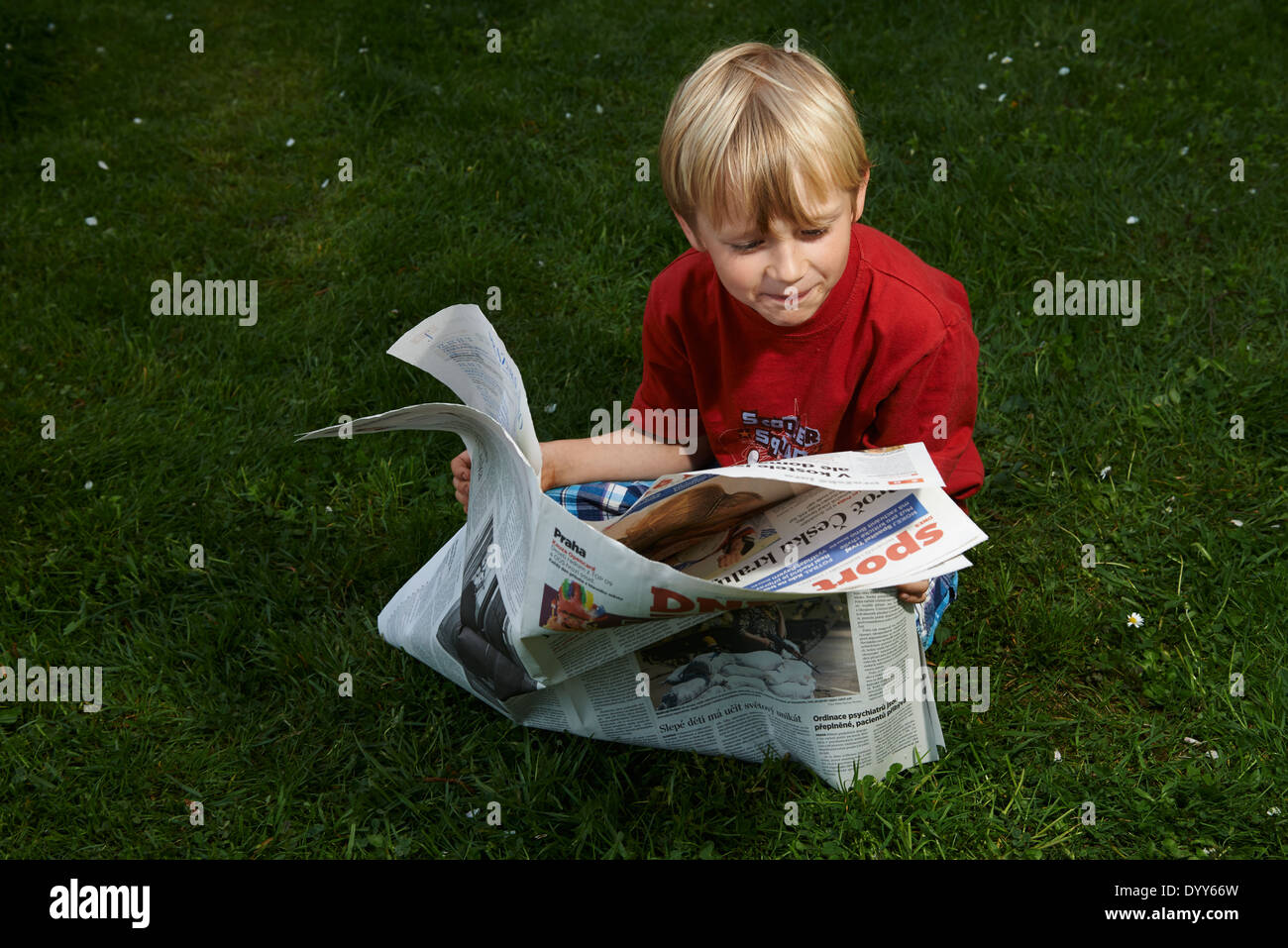 Ein Kind blonde junge liest Zeitung außerhalb am grünen Rasen Stockfoto