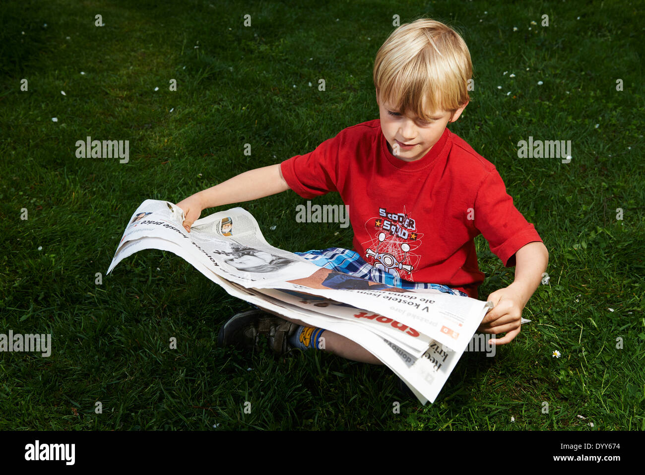 Ein Kind blonde junge liest Zeitung außerhalb am grünen Rasen Stockfoto