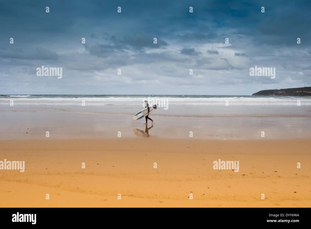 einsamer Surfer zu Fuß an den sehr niedrigen Gezeiten am goldenen Sandstrand mit langes Brett. große Foto. dramatische Gewitterhimmel. Australien Stockfoto