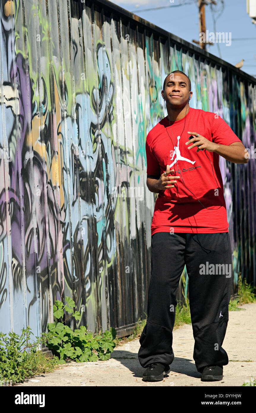 Ein junger Mann, African American, gerne Musik hören über Kopfhörer, tanzen vor Graffitiwand. Stockfoto