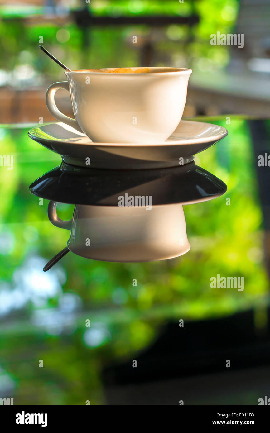Tasse Kaffee am Tisch aus Glas Spiegel reflektieren grünen Sommer Garten Morgensonne Stockfoto