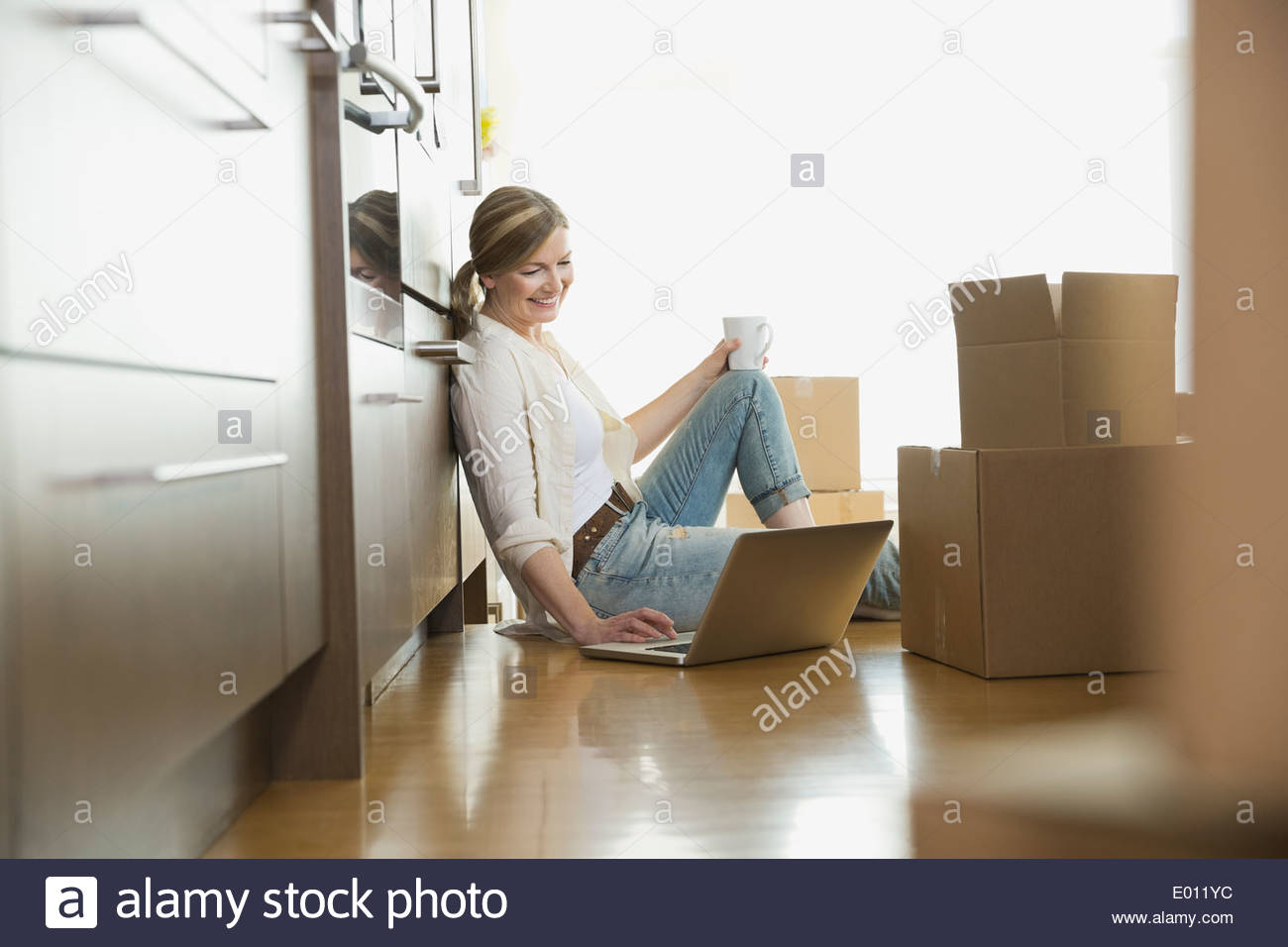 Frau mit Laptop am Boden in der Nähe von Umzugskartons Stockfoto