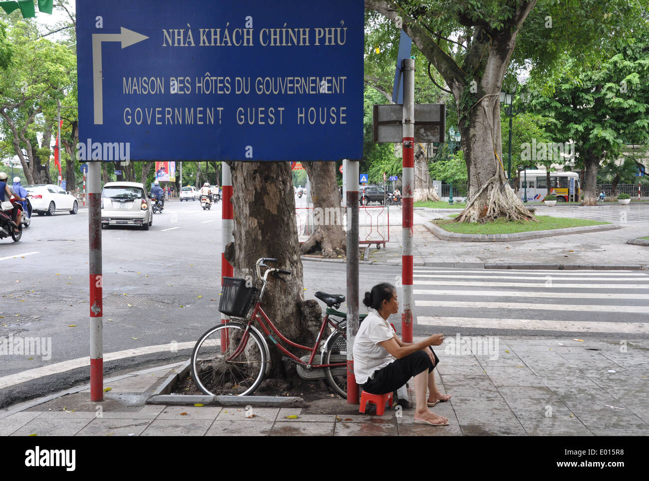 Eine vietnamesische Frau sitzt auf einem kleinen Hocker durch ein großes Schild in Hanoi, Vietnam Stockfoto