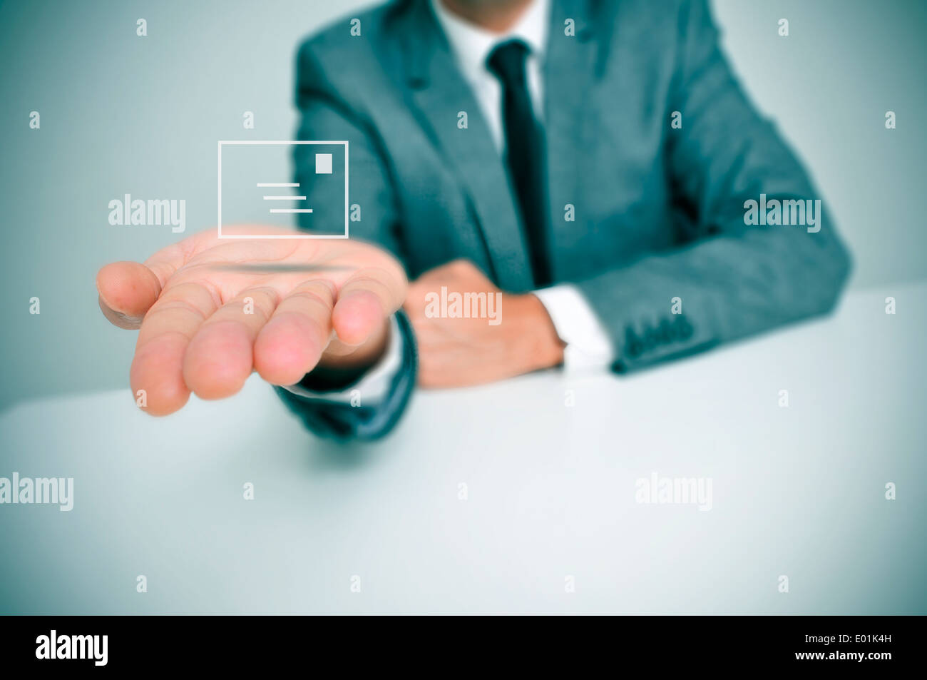 ein Geschäftsmann sitzt in einem Schreibtisch mit einem Briefsymbol in der hand Stockfoto
