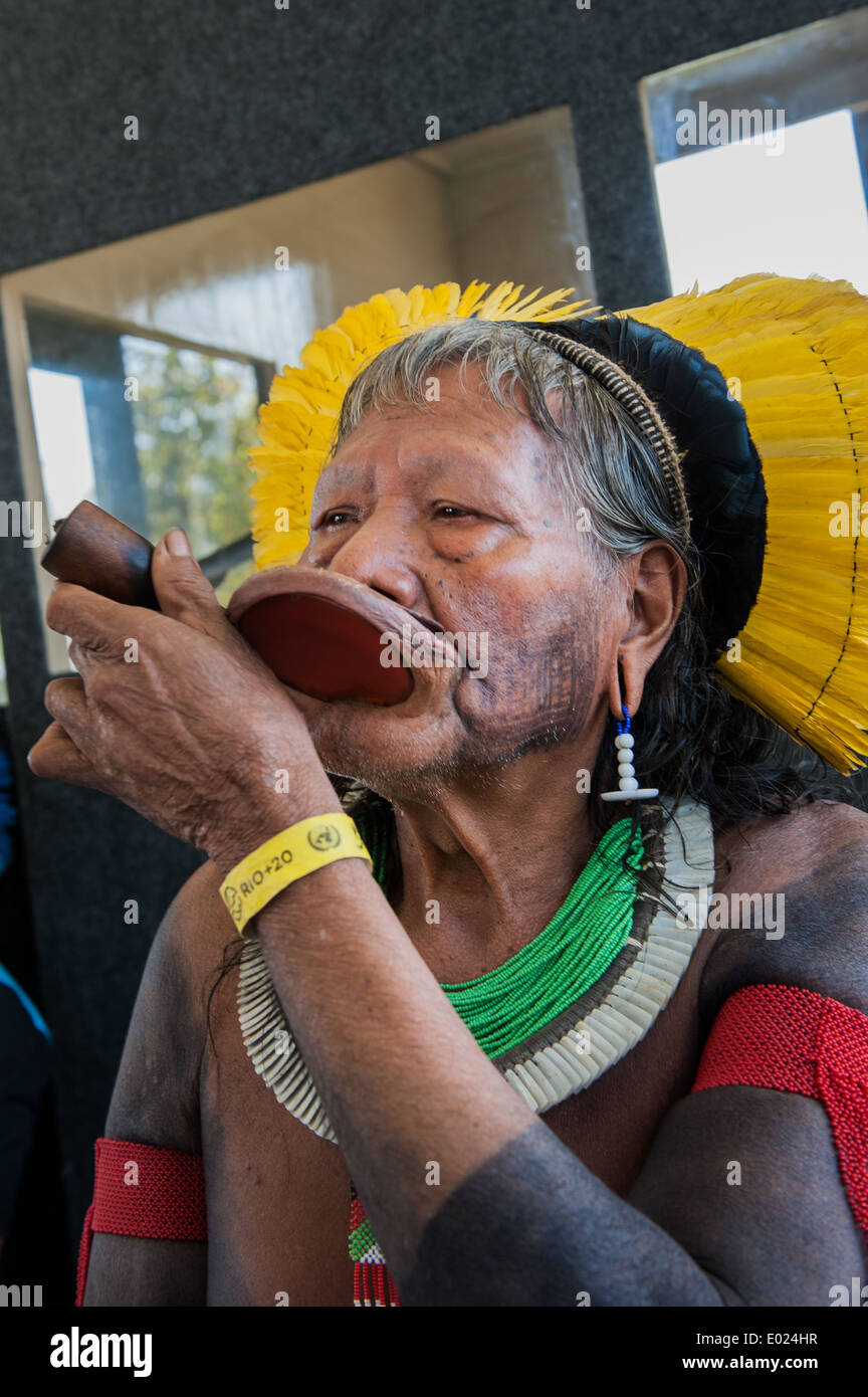 Kayapo Chief Raoni Txucarrhamae raucht seine Pfeife mit Headress und "Rio + 20" gelbe Armband für die Teilnehmer. Die Menschen Gipfel auf der Konferenz der Vereinten Nationen für nachhaltige Entwicklung, Rio De Janeiro, Brasilien. Stockfoto