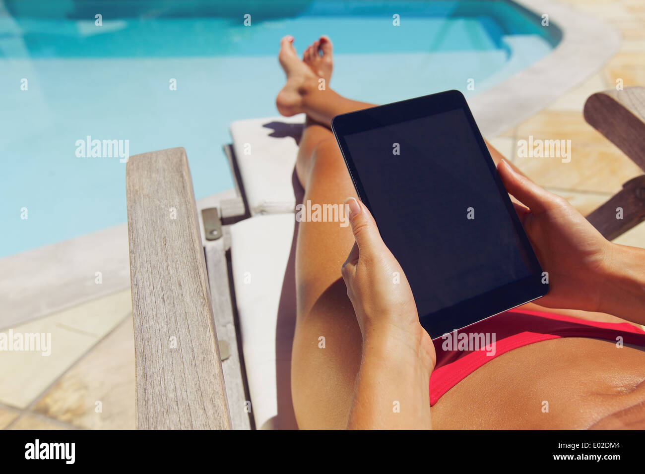 Entspannte Frau liest auf digital-Tablette. Braungebrannte Mädchen Sonnenbaden und halten Touchpad am Pool Stockfoto