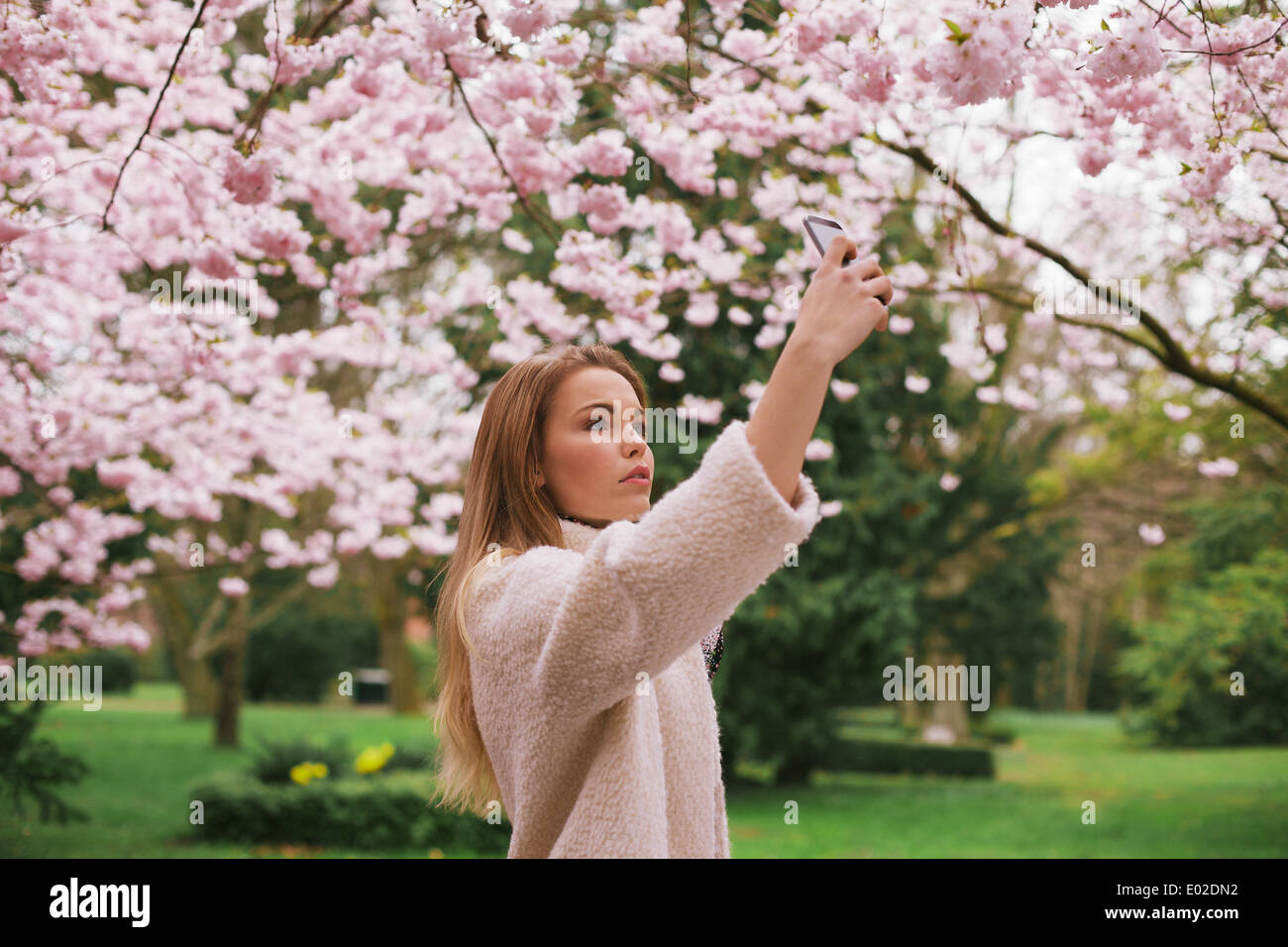 Kaukasische Mädchen malte Blüte Blumen mit ihrem Handy. Attraktive Frau fotografieren Blumen im Frühlingspark Stockfoto