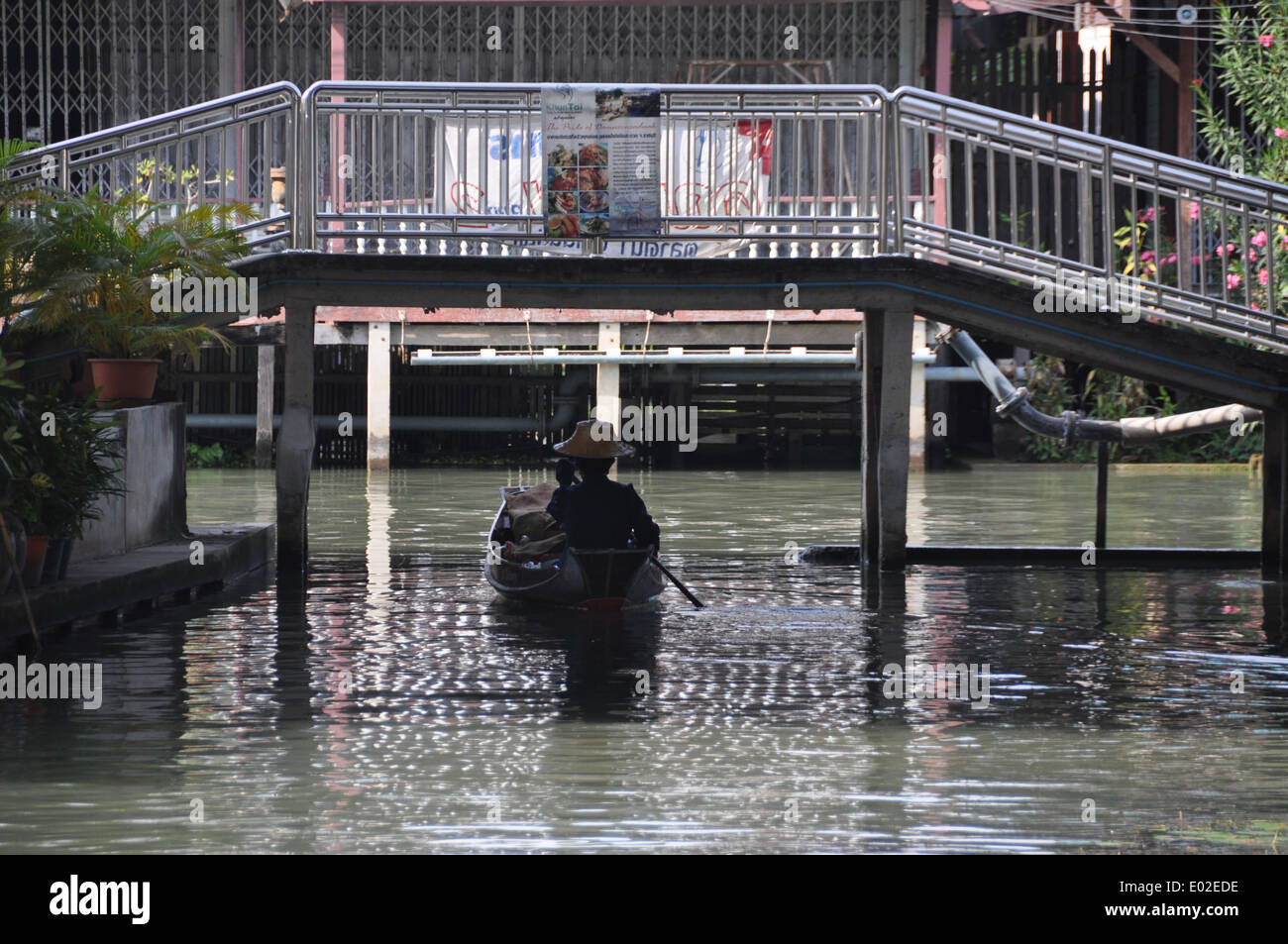 Thai Dame ihr Boot unter einer Fußgängerbrücke zu paddeln. Stockfoto
