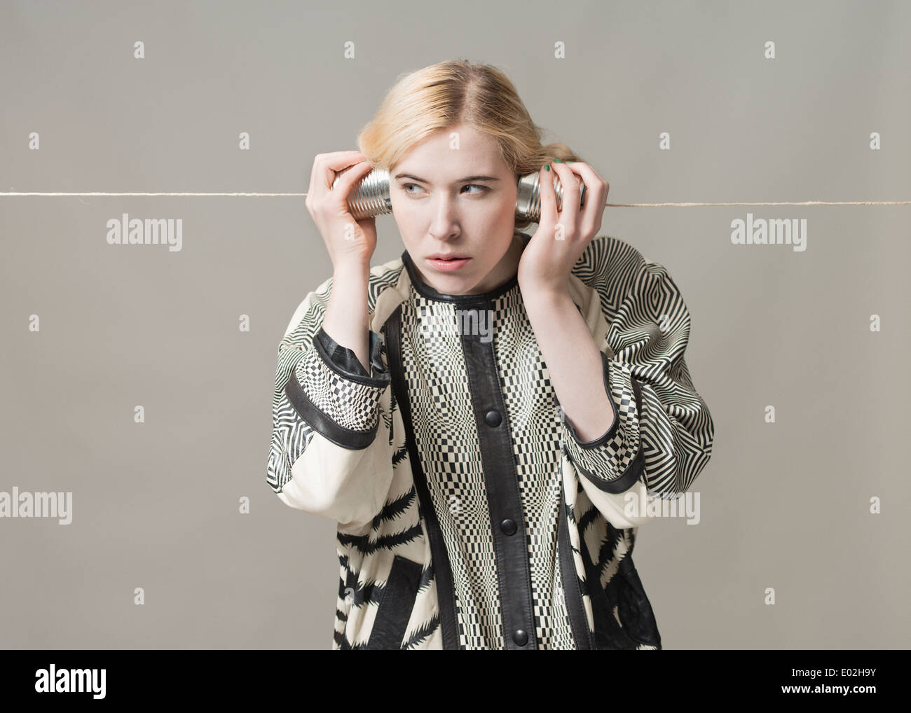 Blonde Frau mit Blechdose Telefon hören. Konzeptbild von Spionage, Überwachung und Kommunikation. Stockfoto