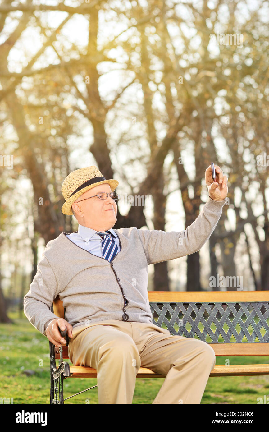 Ein Alter Mann, wobei ein Selbstporträt mit Handy auf Bank im Freien sitzen Stockfoto