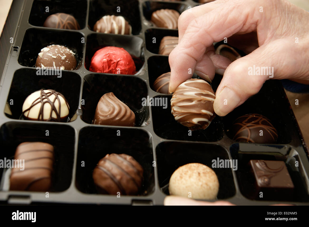 Ältere Frau, die sich dazu eine Schokolade aus einer Schachtel Pralinen Stockfoto