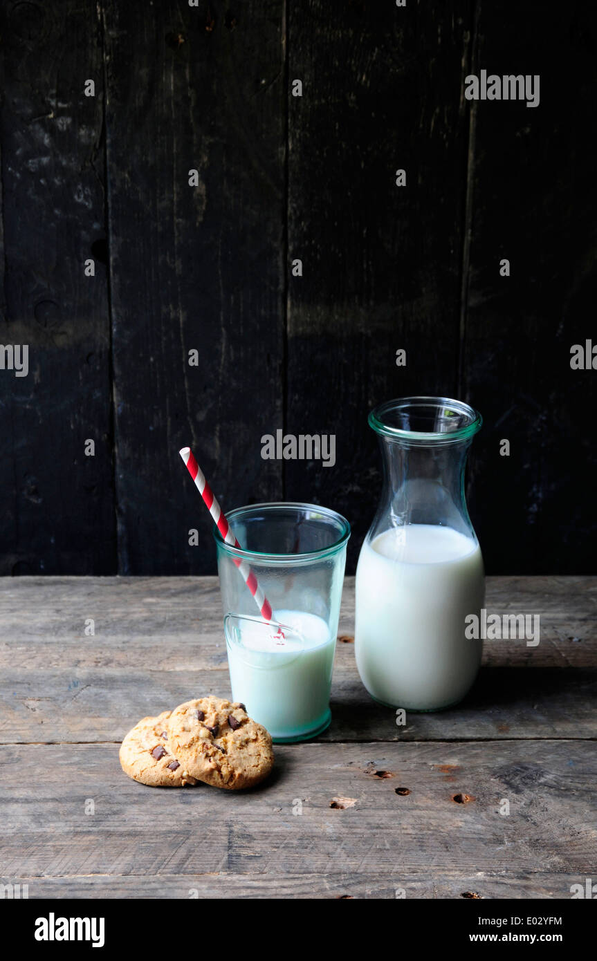 Milchflasche und Glas mit Strohhalm und Keksen auf alten hölzernen Hintergrund Stockfoto