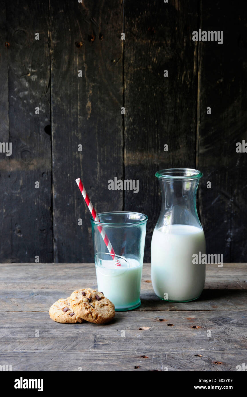 Milchflasche und Glas mit Strohhalm und Keksen auf alten hölzernen Hintergrund Stockfoto