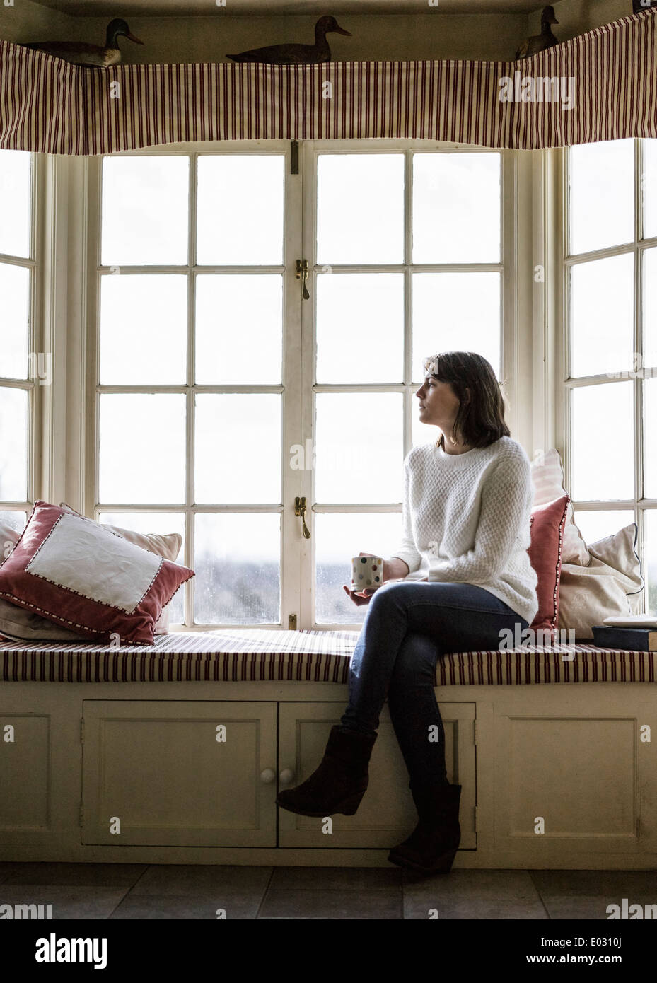 Eine junge Frau sitzt an einem Fensterplatz mit einer Tasse Tee. Stockfoto