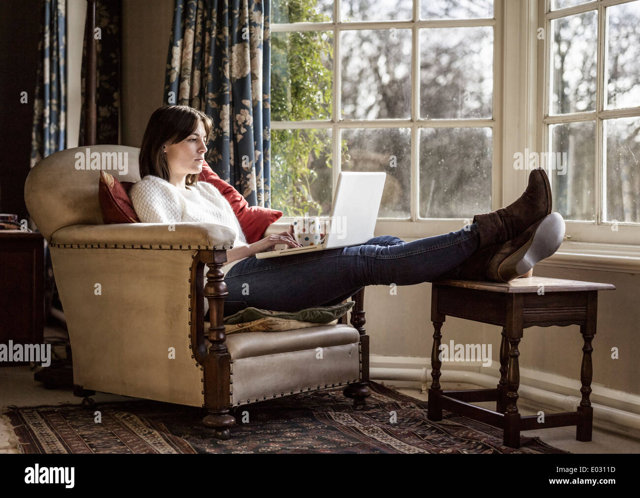 Eine junge Frau mit ihren Füßen mit einem Laptop zu Hause entspannen. Stockfoto